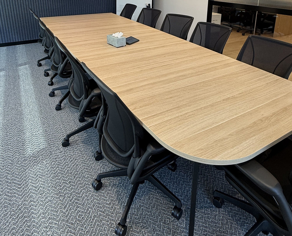 Long oak meeting table with a rounded end and black mesh-back task chairs down both sides