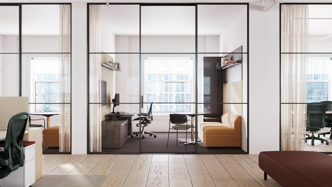 Black Herman Miller Aeron at a dark timber desk inside a glass-walled private office, with three more Aerons in dark green in the surrounding open areas.