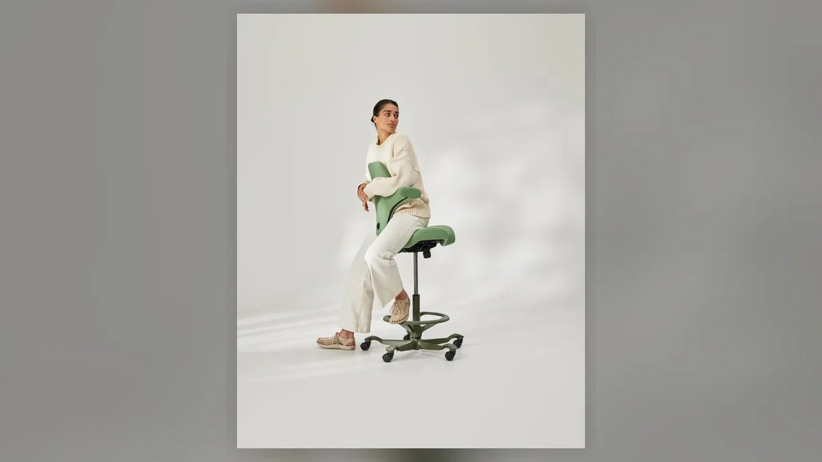 Person working at elevated height on a HÅG Capisco saddle chair, showing the gas lift column and base
