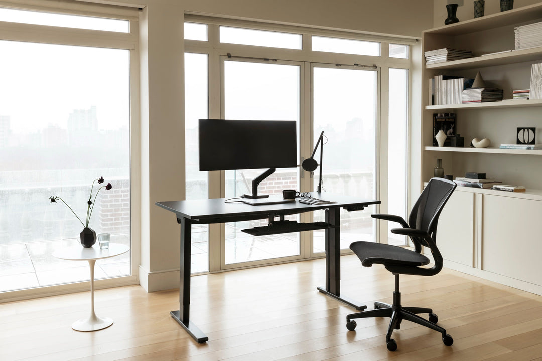 A black ergonomic task chair at a height-adjustable desk with a task light in an Australian office, the kind of purchase claimed under the instant asset write-off