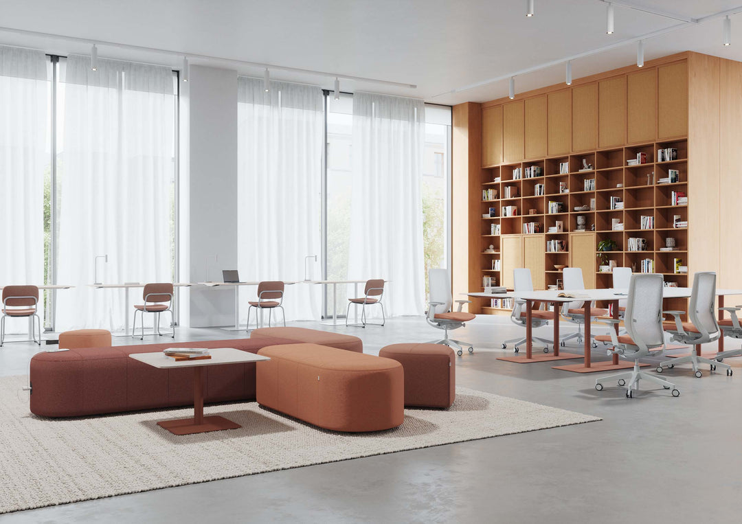 Open-plan office with terracotta Profim Revo modular seating islands on a cream rug and a row of Profim Accis mesh-back task chairs at white desks.