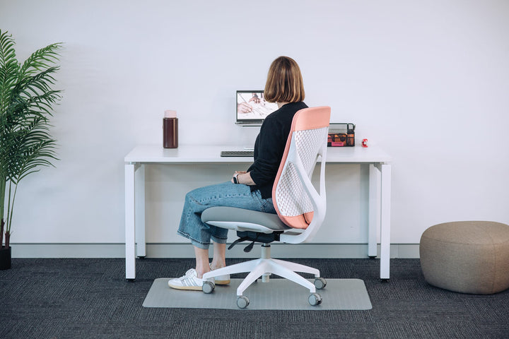 Woman seated at a desk on a white-frame Buro Axon office chair, side view