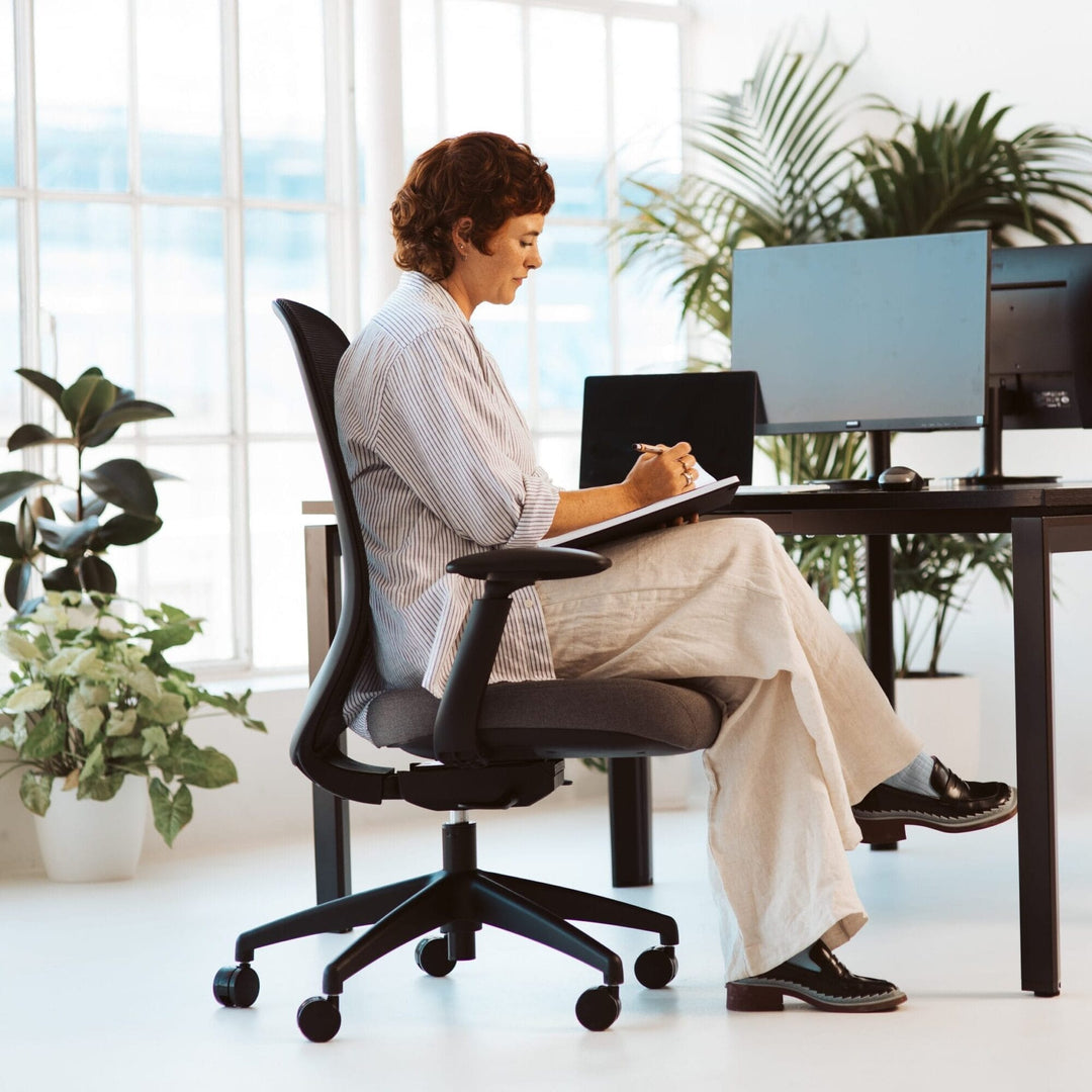 Woman writing while seated on a black-frame Buro Force mesh office chair with arms