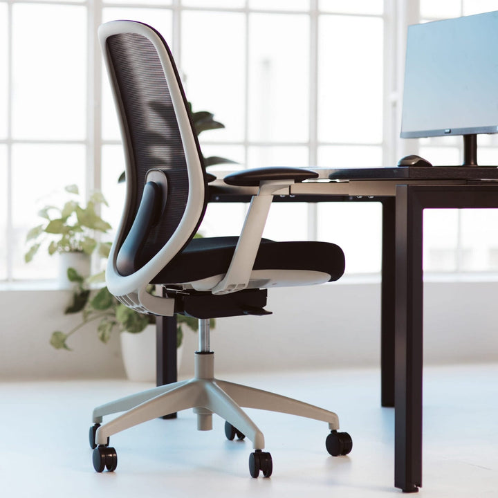 Light grey Buro Force mesh office chair with arms at a black desk in a bright office