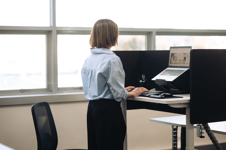 Buro Syntra height adjustable desk 1200 x 600 mm with white frame in use at standing height in an office