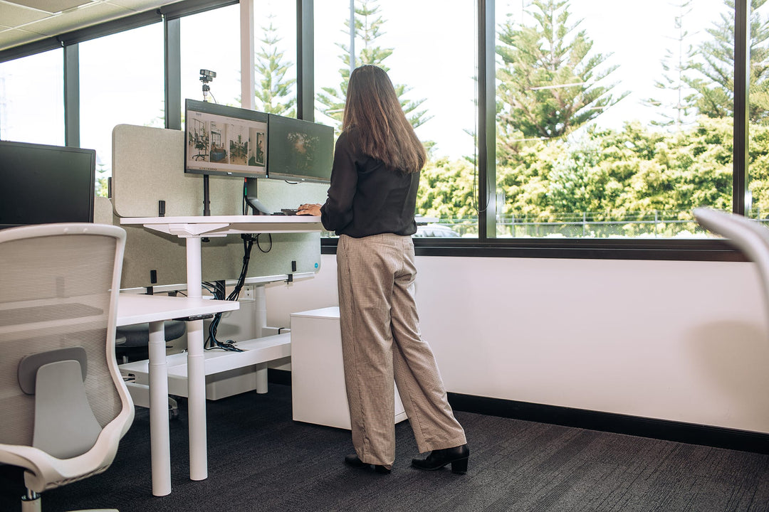 Buro Syntra height adjustable desk with white frame raised to standing height in an office