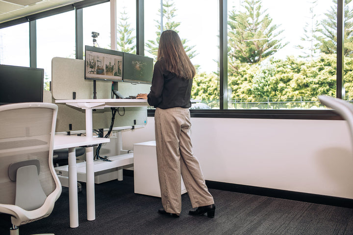 Buro Syntra height adjustable desk with white frame raised to standing height in an office