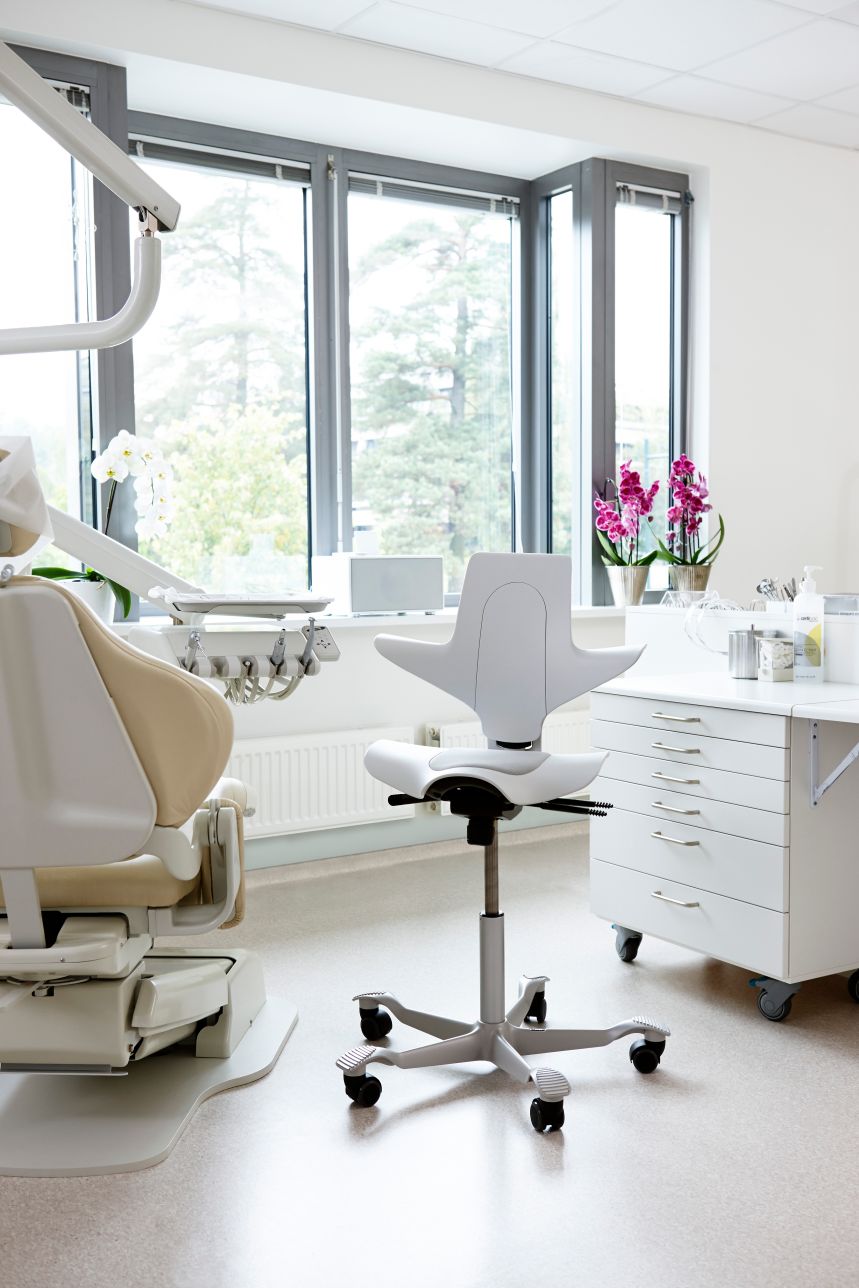 Clinician working at a raised treatment bench on a HÅG Capisco Puls 8010, seat set high with the backrest used as a chest support