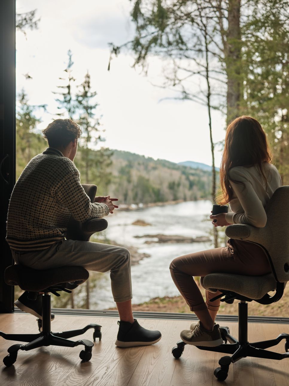 Two people sitting on HAG Capisco chairs looking out at Norwegian river landscape - Chair Dinkum Australia