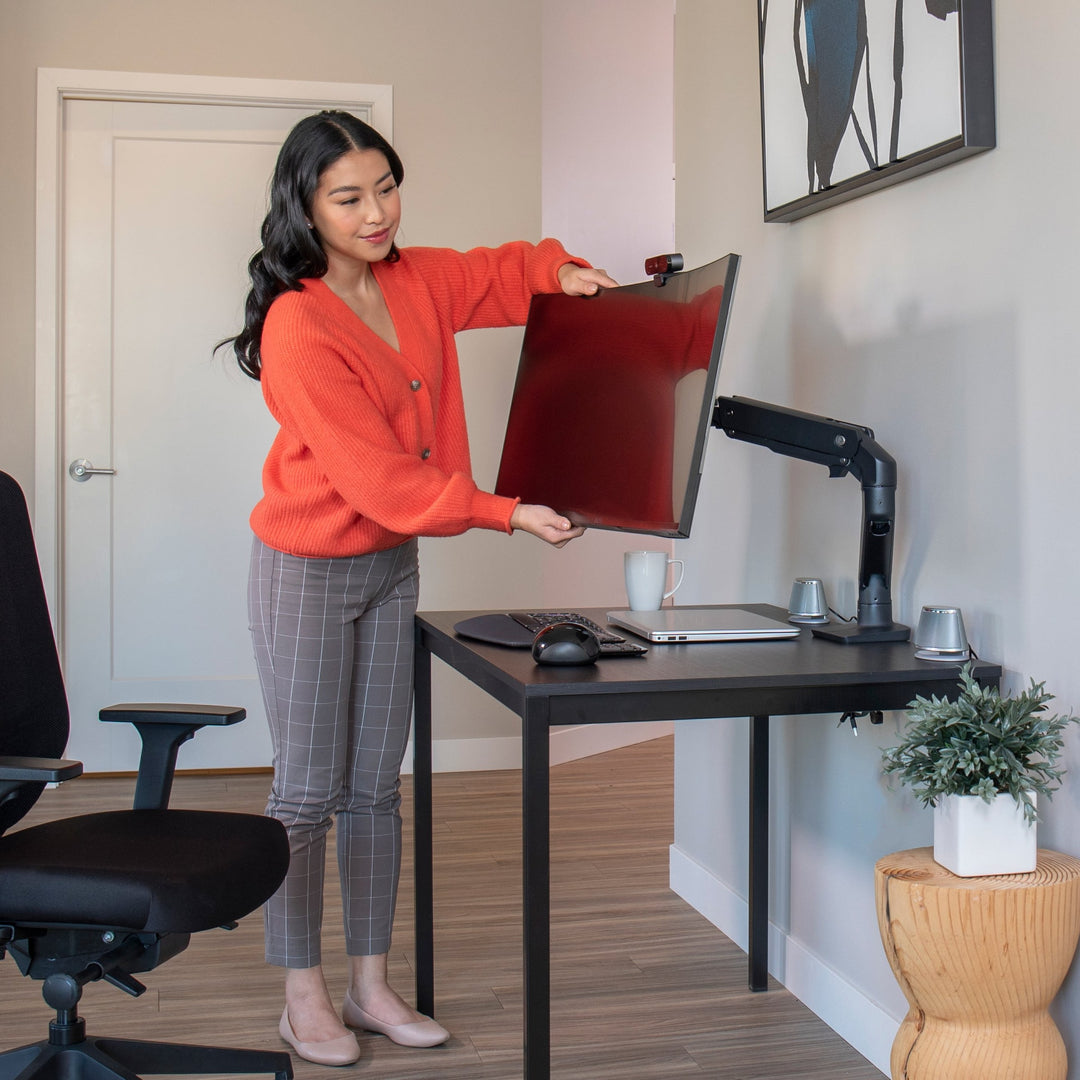 Woman adjusting a large screen on a matte black Ergotron HX Desk Monitor Arm at a home desk