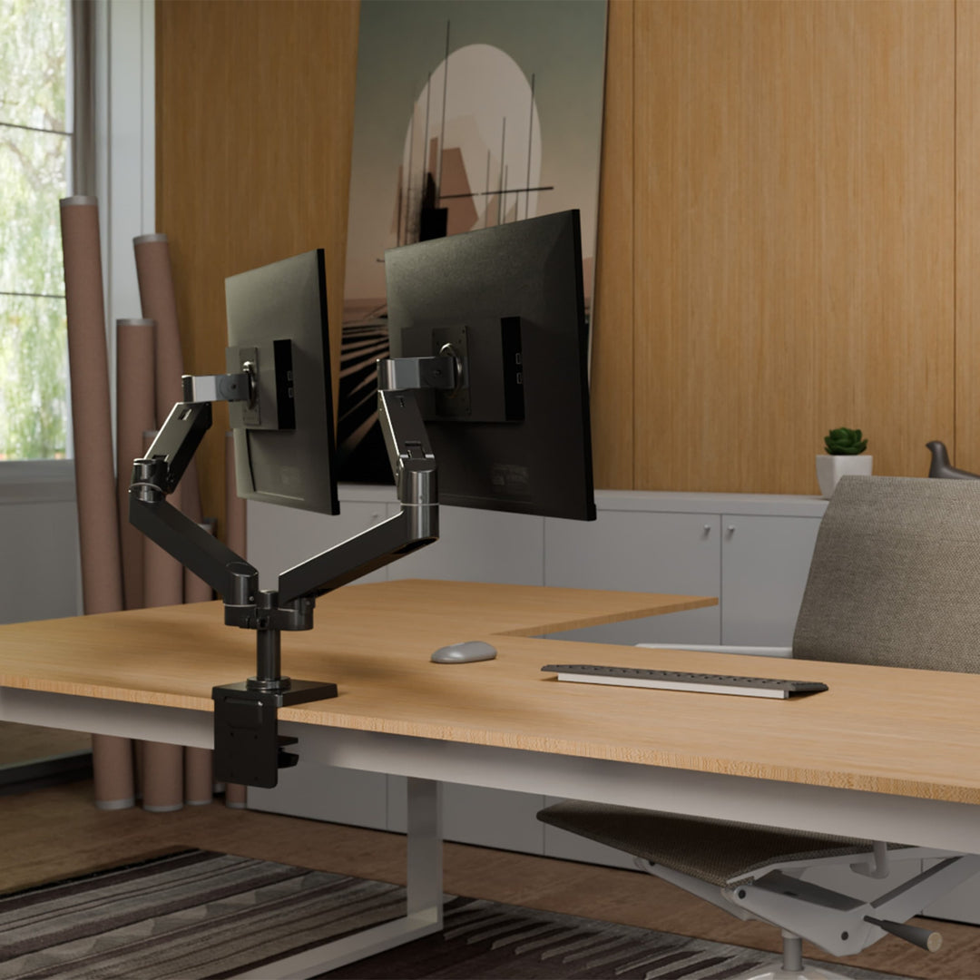 Matte black Ergotron LX Pro Dual Side-by-Side Arm clamped to a desk, holding two screens in a design studio