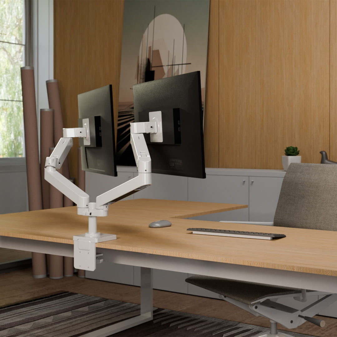 White Ergotron LX Pro Dual Side-by-Side Arm clamped to a desk, holding two screens in a design studio