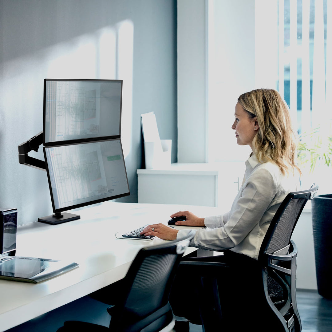 Woman working at a desk with two stacked screens on a matte black Ergotron LX Pro Dual Stacking Arm