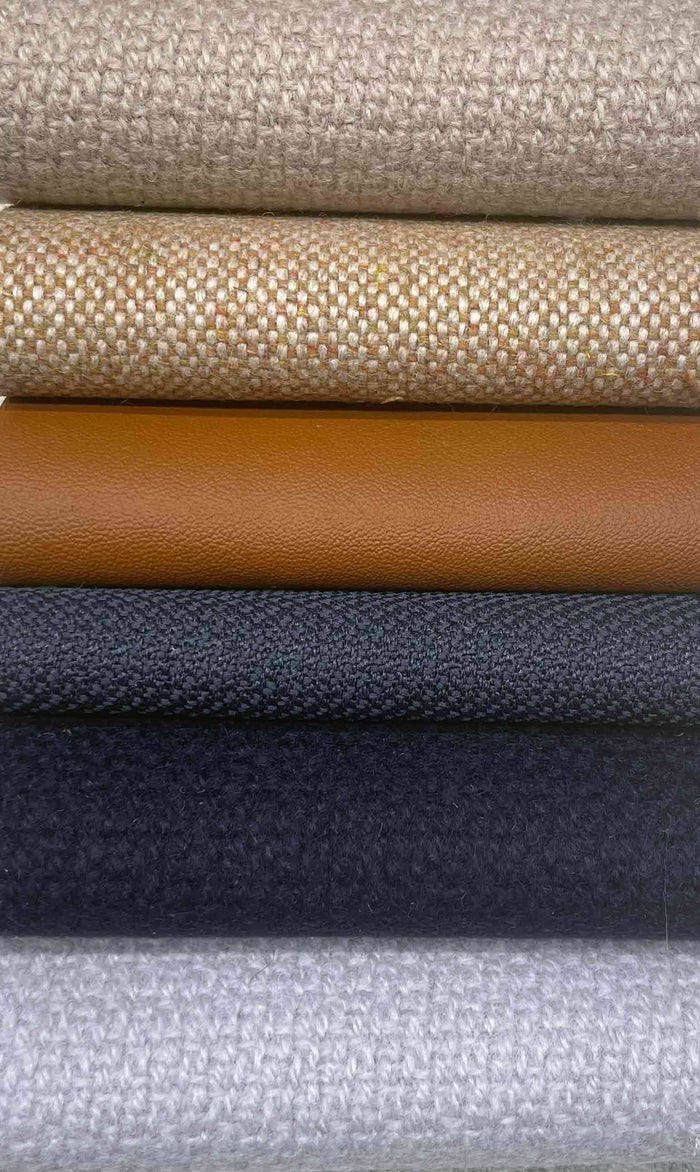 Six upholstery swatches stacked in a close-up row: two beige woven fabrics, tan leather, dark grey weave, navy wool and pale grey weave.