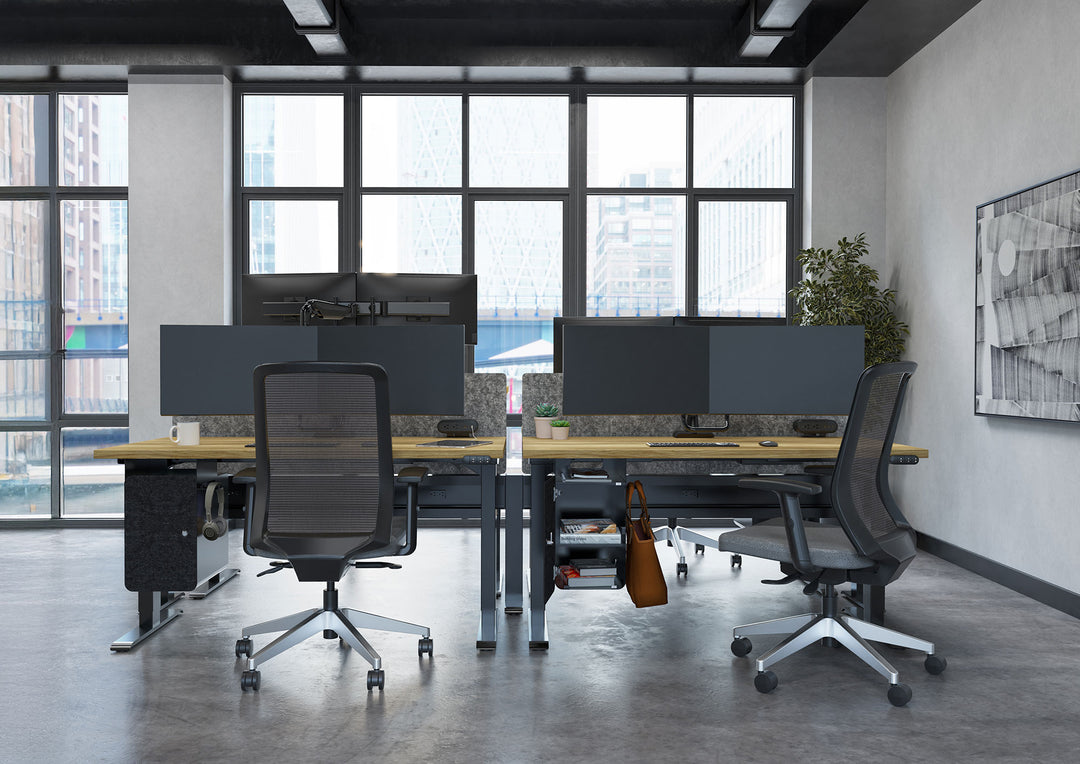 Open office with black HAT Collective E5 dual crossbar monitor arms on a four-desk height-adjustable cluster