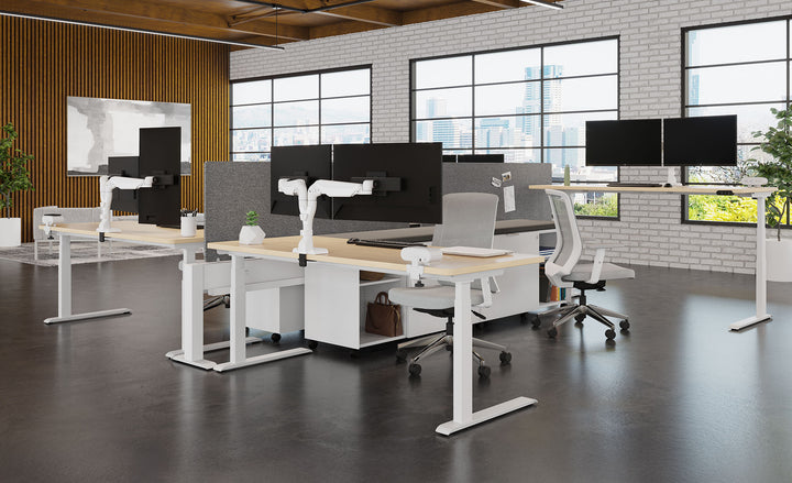 Open office with white HAT Collective E5 dual monitor arms on white height-adjustable desks