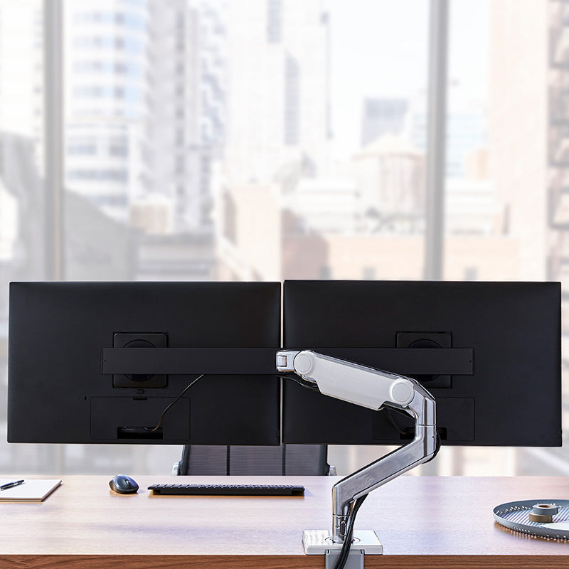 Two monitors on Humanscale M8.1 arms at a desk by a window - Humanscale photograph