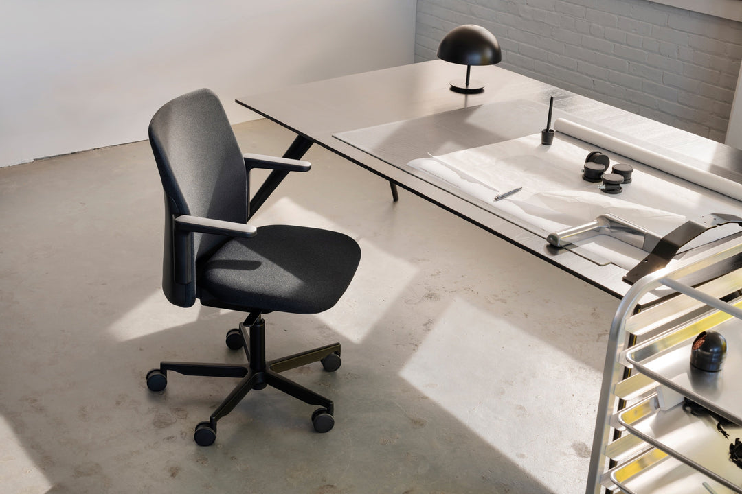 Black Humanscale Path chair with arms beside a long white desk in a sunlit studio