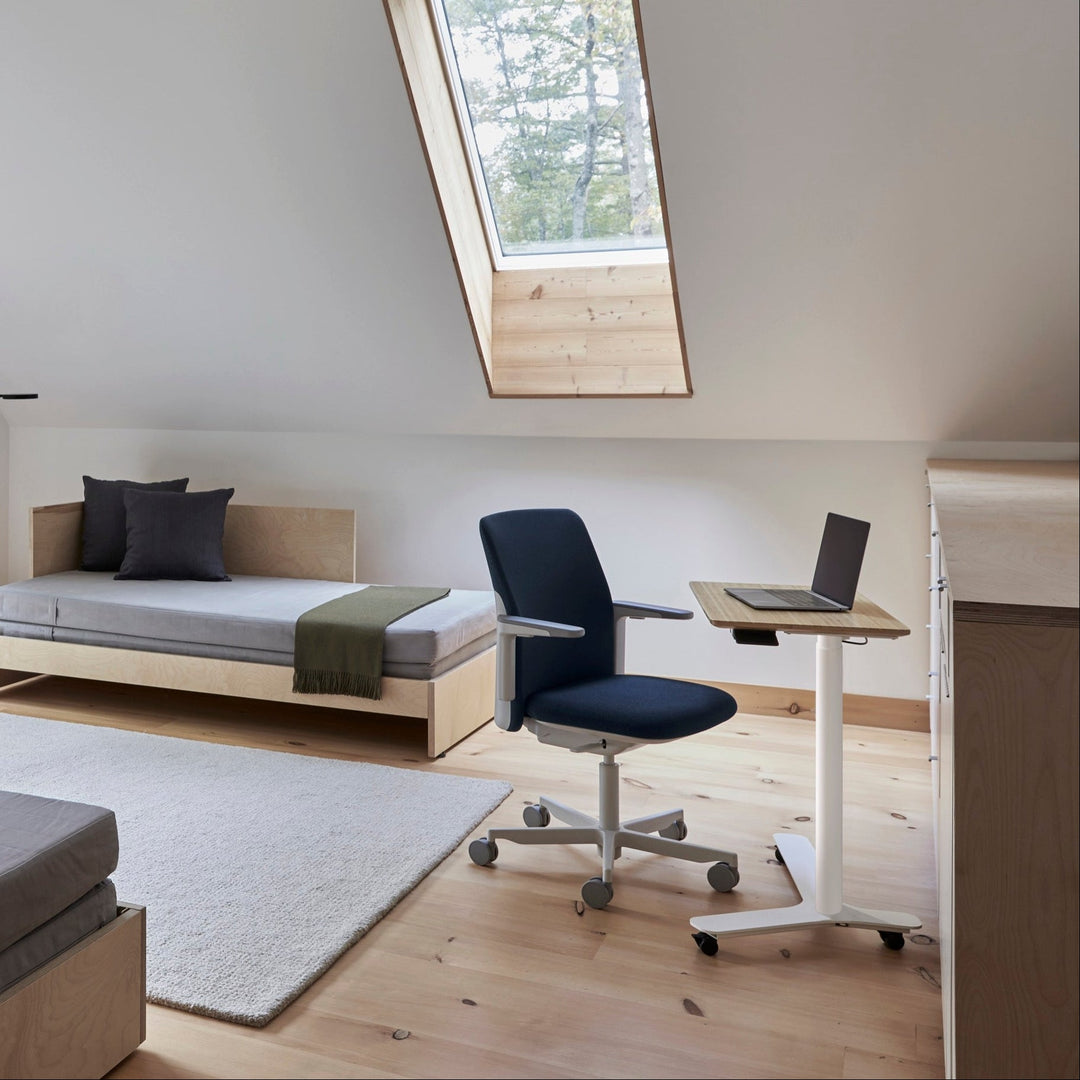 Humanscale Path chair with a dark blue knit back at a small white desk in a sunlit attic home office