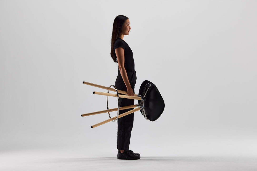 Woman carrying a Humanscale Sedeo stool with maple legs and a black seat