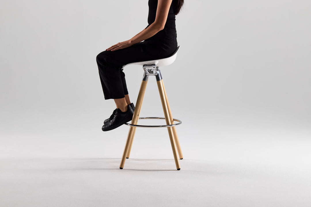 Woman seated on a Humanscale Sedeo bar stool with maple legs, polished frame and white seat