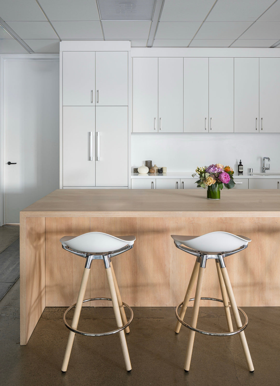 Two Humanscale Sedeo bar stools with maple legs, polished frames and white seats at a pale timber kitchen island