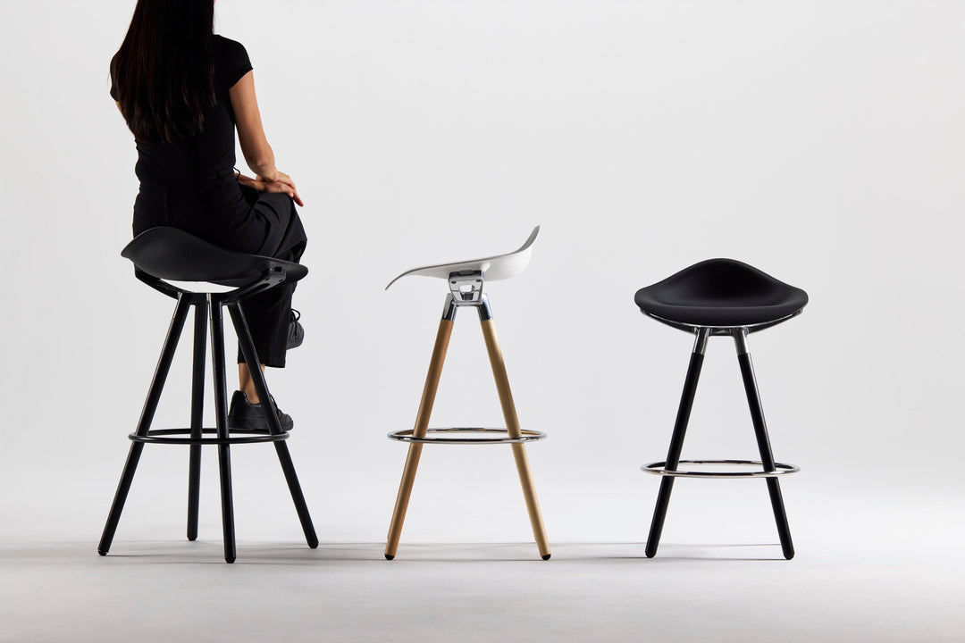 Three Humanscale Sedeo stools in black, maple and white, and all-black finishes, with a woman seated on the left stool