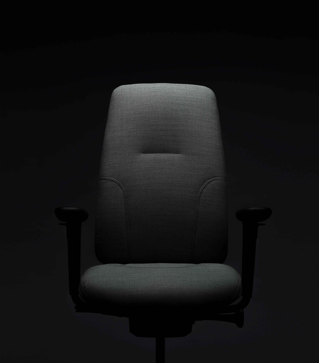 Grey upholstered high-back RH New Logic chair with black armrests, photographed straight on under dramatic lighting against a near-black background.