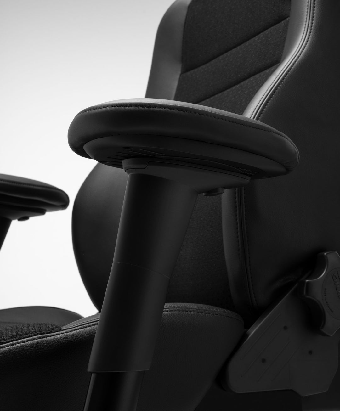 Close-up of an RH Secur24 armrest, its padded leather pad on a tapered post, with the stitched backrest and part of the seat mechanism behind.