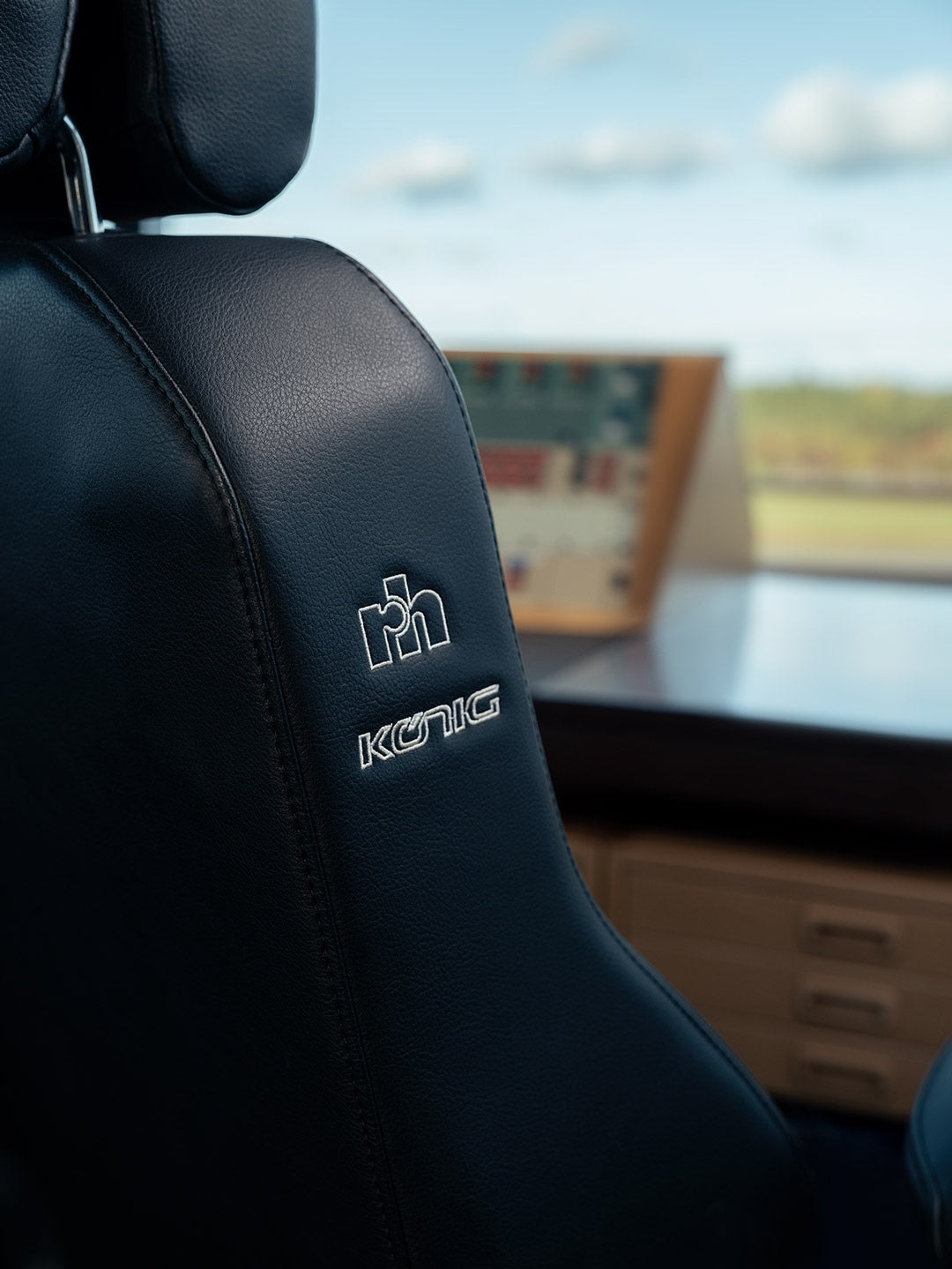 Close-up of the RH Secur24 headrest and backrest in black leather with the RH logo, control tower windows behind - Chair Dinkum Australia