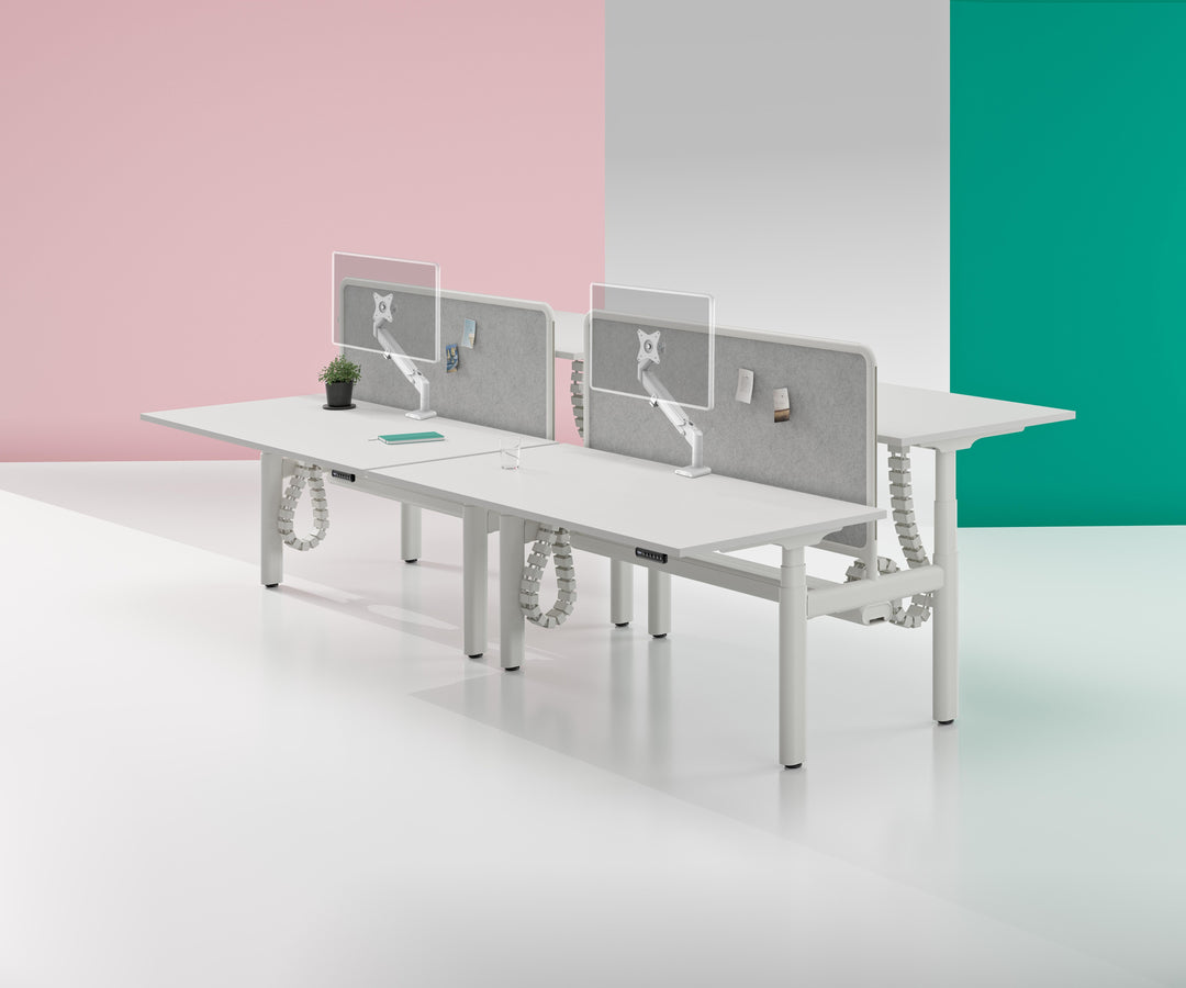 Two white Thinking Works Vader arms on a back-to-back white bench desk run with grey felt dividers, each holding one outlined screen.