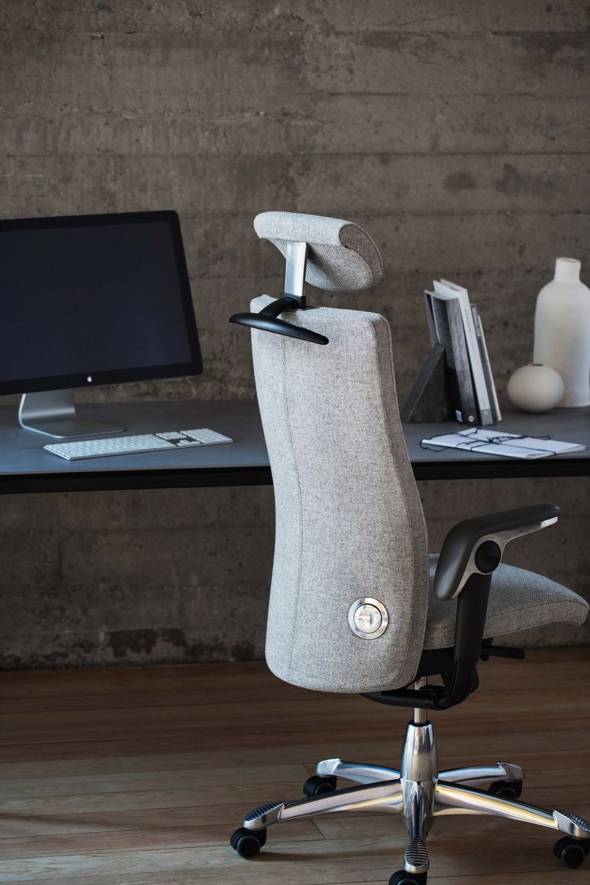 HÅG Tribute 9031 in grey fabric with headrest at a concrete desk, rear three-quarter view - Flokk photograph